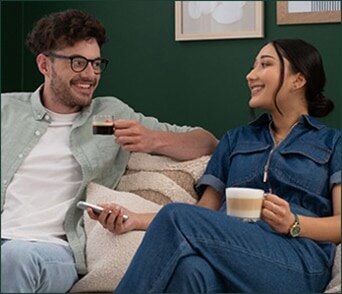 A smiling couple relaxing on a couch, enjoying NESCAFÉ Dolce Gusto coffee together